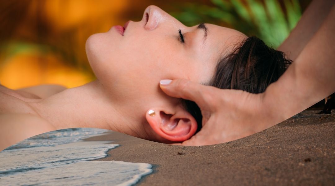 Der Kopd einer Frau wird in einer Einzelsession mit Händen gehalten. Darunter sieht man eine Welle die über den braunen Sandstrand läuft.